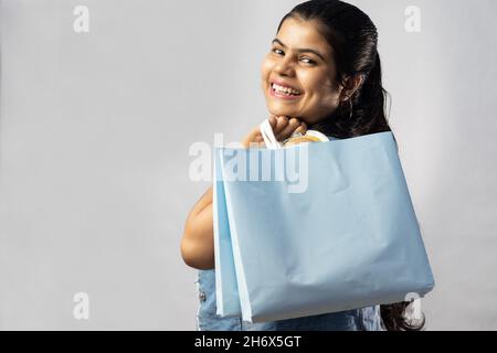 Eine schöne indische Frau in gelbem Kleid mit Einkaufstaschen, die auf weißem Hintergrund zurückblicken Stockfoto