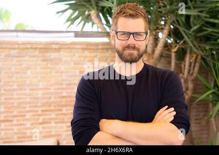 Junger kaukasischer Mann, der eine Brille mit im Freien gefalteten Armen trägt. Stockfoto