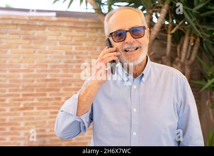 Älterer, gutaussehender Mann, der glücklich und selbstbewusst lächelt. Stehen mit einem Lächeln im Gesicht und reden auf dem Mobiltelefon im Freien. Stockfoto