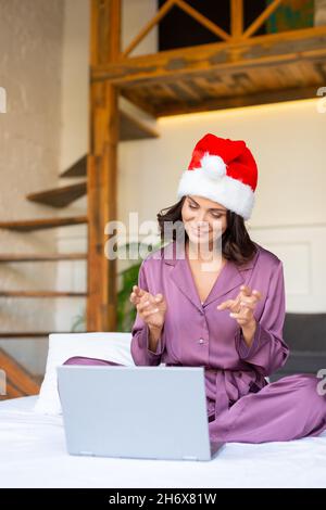 Junge Frau mit Weihnachtsmütze und Pyjama. Neu normal, Quarantäne, Gespräche mit Freunden während eines Videoanrufs. Weihnachten feiern, Distanz sparen, Online-Conferenen Stockfoto