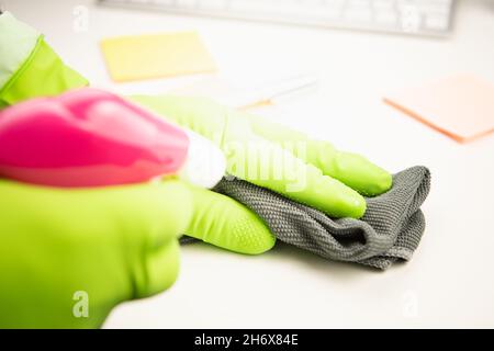 Hand in Schutzhandschuh mit Serviette Reinigung Schreibtisch Büro. Covid-19 Desinfektionskonzept Stockfoto