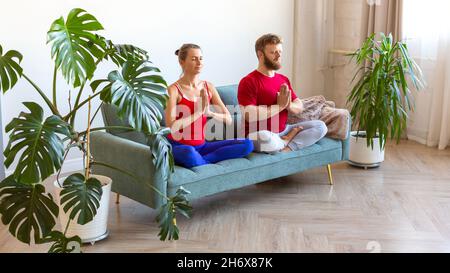 Konzept der psychischen Gesundheit und eines gesunden Lebensstils - Paar mittleren Alters meditiert, während sie auf der Couch sitzt. Formatieren Sie das Foto 16 x 9. Stockfoto