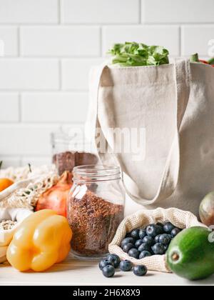 Frisches Gemüse und Obst in Öko-Baumwollbeuteln und Getreide in Gläsern auf dem Tisch in der Küche. Zero Waste Shopping-Konzept. Vorderansicht. Speicherplatz kopieren. Stockfoto