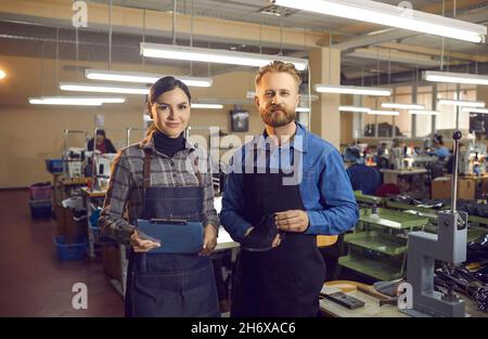 Portrait von zwei glücklichen Schuhfabrikarbeitern, die in der Werkstatt stehen und die Kamera betrachten Stockfoto