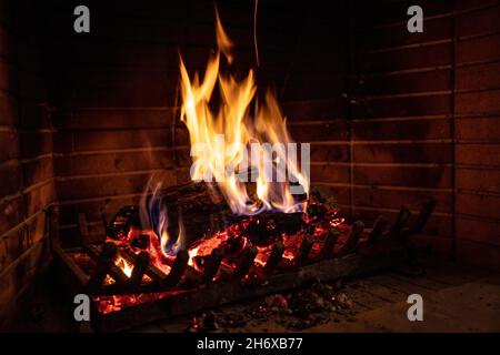 Kamin brennendes Feuerholz. Lagerfeuer, Feuerflammen auf Holzstämmen, Backstein Hintergrund. Gemütliches Zuhause zu Weihnachten. Winterurlaub Entspannung und warm Stockfoto