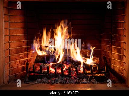 Kamin brennendes Feuerholz. Lagerfeuer, Feuerflammen auf Holzstämmen, Backstein Hintergrund. Gemütliche Zimmereinrichtung zu Weihnachten. Winterurlaub Entspannung und warm Stockfoto