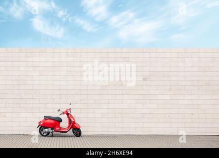 Einsamer roter Roller gegen weiße Wand, urbaner Minimalismus mit Vintage-Motorrad Stockfoto