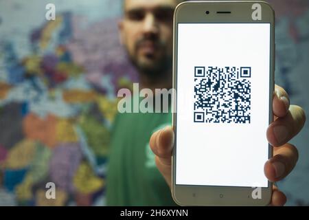 Ein Mann mit einem Smartphone auf dem Bildschirm QR-Code des Impfzertifikats Covid-19. Elektronischer Reise-Impfpass. Im Hintergrund ist ein Stockfoto