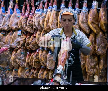 Frau, die spanischen Iberico-Schinken mit geräucherten Schinkenbeinen in der Supermarktdisplakette, Andalusien, Spanien, schnitzt Stockfoto