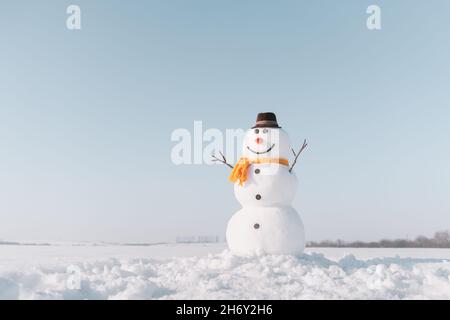 Lustige Schneemann in stilvollen braunen Hut und gelben Skalf auf schneebedeckten Feld. Blauer Himmel auf dem Hintergrund Stockfoto