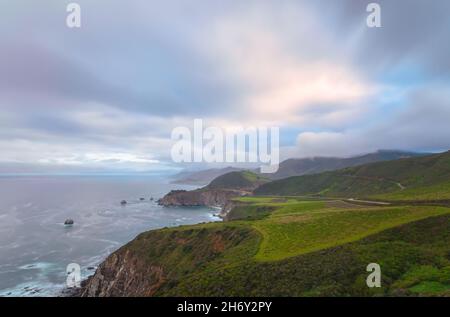 Eine atemberaubende Küstenlandschaft mit einem dramatischen Himmel voller flauschiger, weißer Wolken, zerklüfteter Klippen und grüner Hügel in Big Sur, Kalifornien. Stockfoto