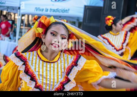 2021 10 09 Tulsa USA schöne hispancing Girls lächeln, als sie in einem Wirbel gelber Dessen auf einem Straßenfestival tanzt - Bewegung blau und Boksh Backgr Stockfoto