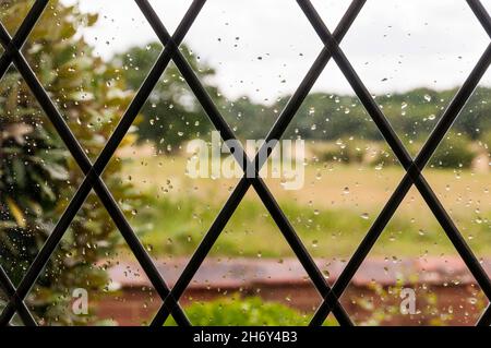 Unfokussierte Landschaft durch Regentropfen auf rautenverglasten Fenstern der Hütte. Stockfoto