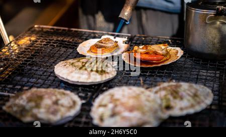 Händler verkaufen Jakobsmuscheln in Tsukiji Fischmarkt. Mann, der in Einzelhandelsgeschäften und Restaurants waren in Meeresfrüchten zubereitet, carter der Öffentlichkeit in Tokio. Berühmte m Stockfoto