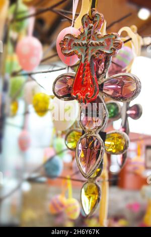 Keramische Kreuzsymbole und Ostereier, die an Zweigen mit unscharfem Bokeh-Hintergrund hängen Stockfoto