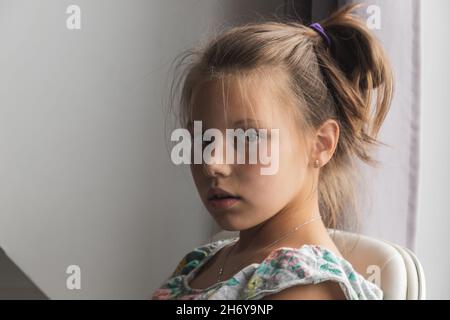 Natürliche Nahaufnahme Porträt von kleinen kaukasischen Mädchen sitzt in der Nähe des Fensters in einem Raum Stockfoto