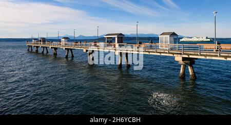 Edmonds, WA, USA - 17. November 2021; Fischerpier in Edmonds Washington mit einer staatlichen Autofähre, die dahinter vorbeifährt. Der Tag hat hohe Wolken Stockfoto