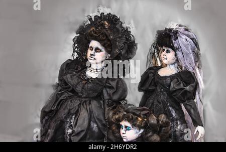 Drei gruselige Gothic-Puppen in schwarzen viktorianischen Kleidern - eine ist eine Braut - mit todaussehender Haut und seltsamen Augen Stockfoto