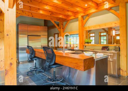 Insel mit Edelstahl-Arbeitsplatte und geölten Kiefernholz Bar mit schwarzem Kunststoff und Leder hohe Rückenstühle in der Küche im Holzrahmen Haus Stockfoto