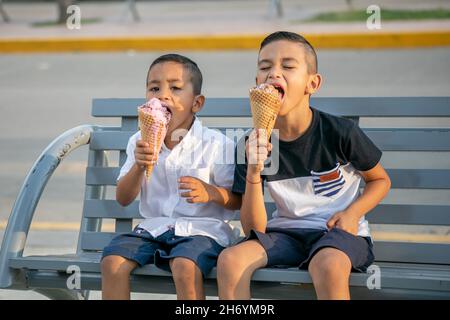 Hispanisch fröhliche Kinder sitzen auf einer Bank in einem Park und essen Eis Stockfoto