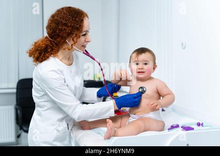 Eine rothaarige Ärztin untersucht das kleine Kind weniger als ein Jahr lang in einer modernen Klinik. Kinderarzt während der Untersuchung Baby im Krankenhaus Stockfoto