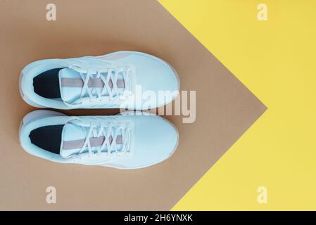 Weiße Sneakers auf beige-gelbem Hintergrund. Sport- und Fitnesskonzept. Draufsicht, flach liegend. Stockfoto