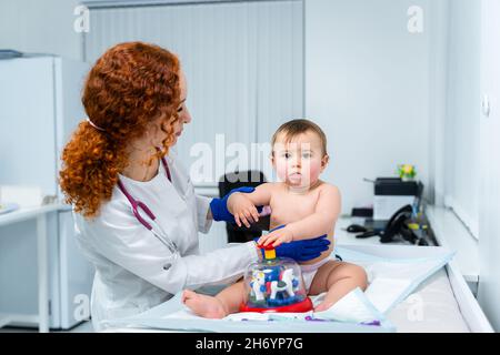 Eine rothaarige Ärztin untersucht das kleine Kind weniger als ein Jahr lang in einer modernen Klinik. Kinderarzt während der Untersuchung Baby im Krankenhaus Stockfoto