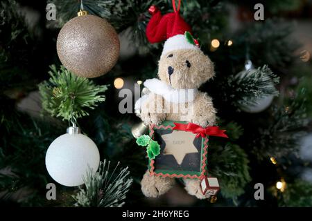 Teddybär hält an der Hoffnung fest, mit Glitzerkugeln, die am Weihnachtsbaum hängen Stockfoto