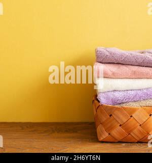 Stapel von Badetüchern im Korb auf Holztisch. Gelber Hintergrund. Platz kopieren Stockfoto