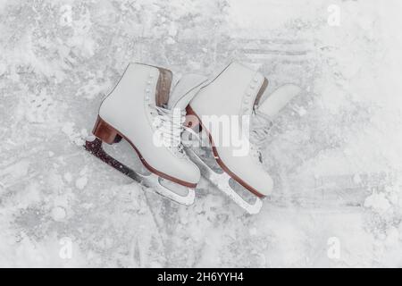 Eiskunstlauf Frauen Schlittschuhe liegen draußen auf weißem gefrorenem Eis Draufsicht Textur Hintergrund. Wintersport Ausrüstung im Freien Stockfoto