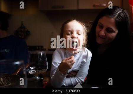 Ein Mädchen isst in einem Landhaus Käse mit blauem Schimmel in den Armen ihrer Mutter. Stockfoto