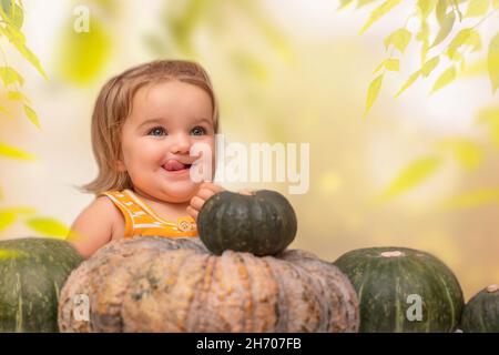 Das Kind sitzt am Tisch mit der Kürbisernte im herbstlichen Hinterhof Stockfoto