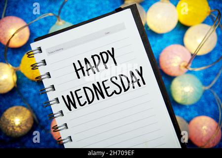 Happy Wednesday Text Notizblock Mockup und LED-Baumwollkugeln Dekoration auf blauem Bokeh Hintergrund Stockfoto