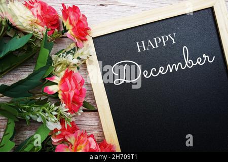 Fröhlicher Dezember-Text auf schwarzem Grund mit Blumenstrauß auf Holzhintergrund verziert Stockfoto