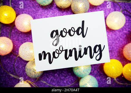 Guten Morgen Text auf Papier Karte Draufsicht auf lila Bokeh Hintergrund Stockfoto