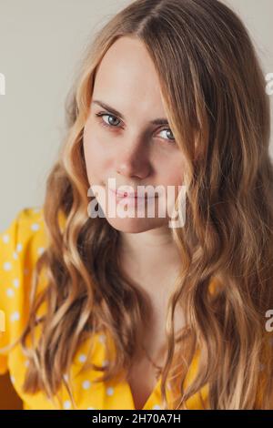Porträt einer schönen lächelnden jungen blonden Frau mit langen lockigen Haaren in Retro-gelbem Kleid, Blick auf die Kamera. Stockfoto