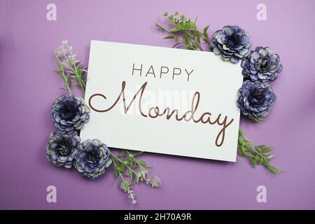 Happy Monday Typografie Text mit Blumen auf violettem Hintergrund Stockfoto