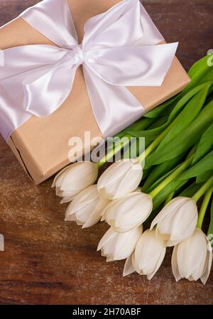 Schöne weiße Tulpen und Geschenkbox mit weißem Ribbonauf dem Holzhintergrund gebunden Stockfoto