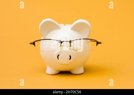 Nahaufnahme eines Sparschweines mit einer Brille auf dem gelben Hintergrund. Das Symbol des Sparens von Geld und Wohlstand finanziell. Stockfoto