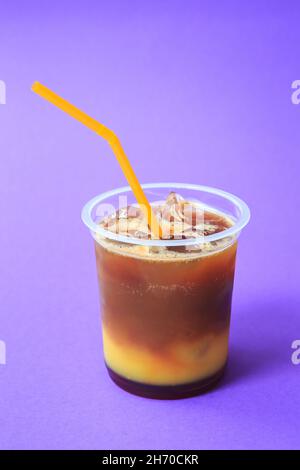 Ein Glas mit orangefarbenem Kaffeecocktail, einem kalten erfrischenden Getränk oder einem Getränk mit Eis auf violettem Hintergrund Stockfoto