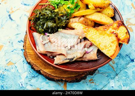 Stücke von gesalzenem Hering mit gebackenen Kartoffeln und Toast. Stockfoto