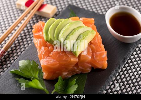 Sushi mit Lachs-Tartare und Avocado-Scheiben, serviert mit Sojasauce auf schwarzem Steinbrett im japanischen Restaurant Stockfoto