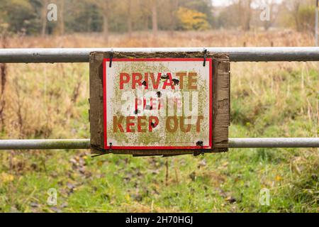 Ein schmutziger Privatperson Bitte halten Sie ein Schild mit Einschusslöchern an einem Metalltor zu einem Feld in der Nähe von Wäldern ab. Stockfoto