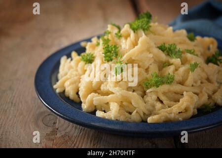 Hausgemachte Spätzle, deutsche Eiernudeln mit Käse serviert mit Petersilie garniert auf einem blauen Teller und einem rustikalen Holztisch, ausgewählter Fokus, enge Tiefe Stockfoto