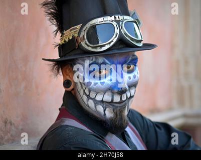 Kostümierter junger mexikanischer Yucatecan-Mann mit gruseliger blauer Gesichtsbemalung und schwarzem Zylinderhut blickt auf den Zuschauer am Tag der Toten (Día de los Muertos). Stockfoto