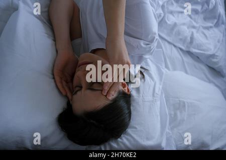 Unglücklich nachdenkliche junge Frau, die Hände auf der Stirn hält, sich traurig einsam liegend im Bett allein versuchen zu schlafen, denken an Problem, Ängste Stockfoto
