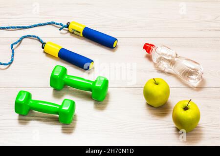 Skipping Rop und Hanteln für Fitness, eine Flasche Wasser und Äpfel in einem Raum oder ein Fitnessstudio auf dem grauen Boden. Draufsicht. Stockfoto