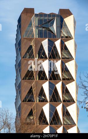 Ein Turm in Form eines goldenen Kristalls mit Spiegel und glitzernder Glasfassade an einem hellen, sonnigen Tag vor einem blauen Himmel. Selektiver Fokus. Urban lan Stockfoto