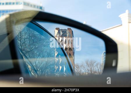 Der Blick vom Auto durch den seitlichen Rückspiegel auf den goldenen Kristallturm gegen den blauen Himmel an einem sonnigen Tag. Selektiver Fokus. Urbane Landschaft Stockfoto