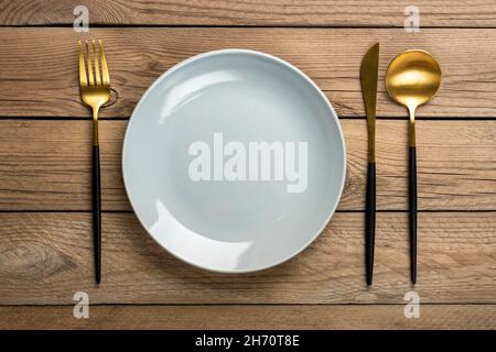 Leere runde graue Platte, Gabel, Messer, Löffel auf Holztisch Draufsicht flache Teller zum Frühstück, Mittag- oder Abendessen Mock up. Stockfoto